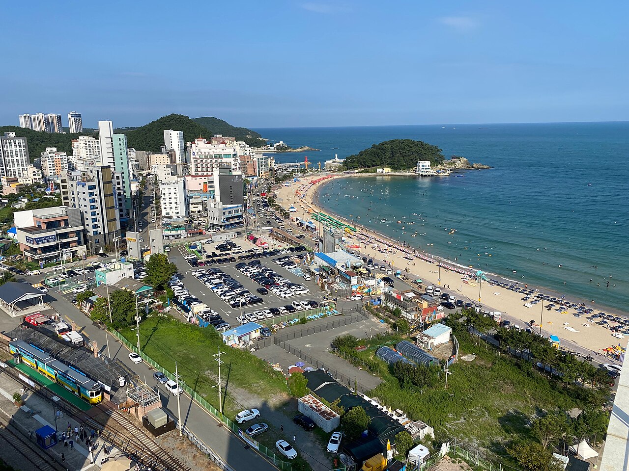 Curving Songjeong shoreline with beach umbrellas and a wooded headland